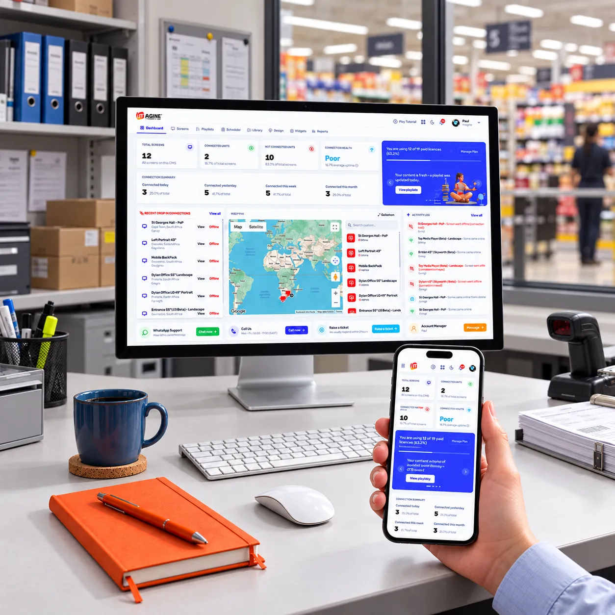 The Imagine digital signage dashboard open on a desktop monitor and a mobile phone in a retail back office
